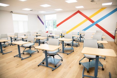 Modern classroom with movable desks and chairs, featuring colorful diagonal wall stripes. Designed for flexible learning and collaboration.
