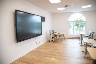 Modern classroom featuring a large screen on one wall, desks and chairs arranged for learning, and a window allowing natural light.