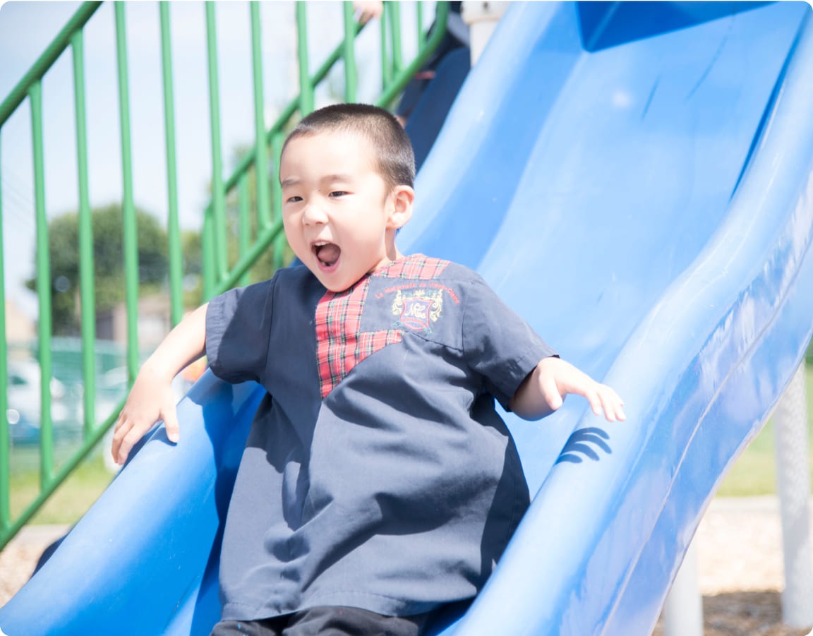 Joyful child sliding down a blue playground slide, grinning widely, enjoying a sunny day outdoors. Captures the essence of childhood play.