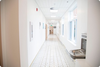 Bright, modern hallway with large windows, featuring a water fountain and minimalist decor, enhancing accessibility and comfort.