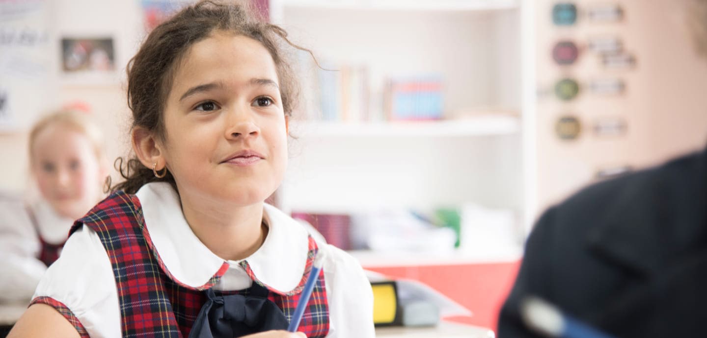 A young girl in a school uniform attentively engages in conversation, highlighting student interaction in a classroom setting.