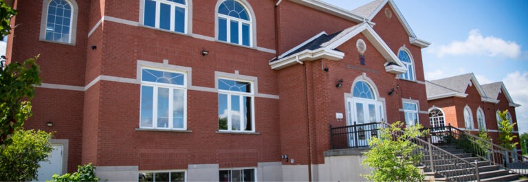 Red brick building with large windows and a prominent entrance. The structure features decorative architecture and is surrounded by greenery.