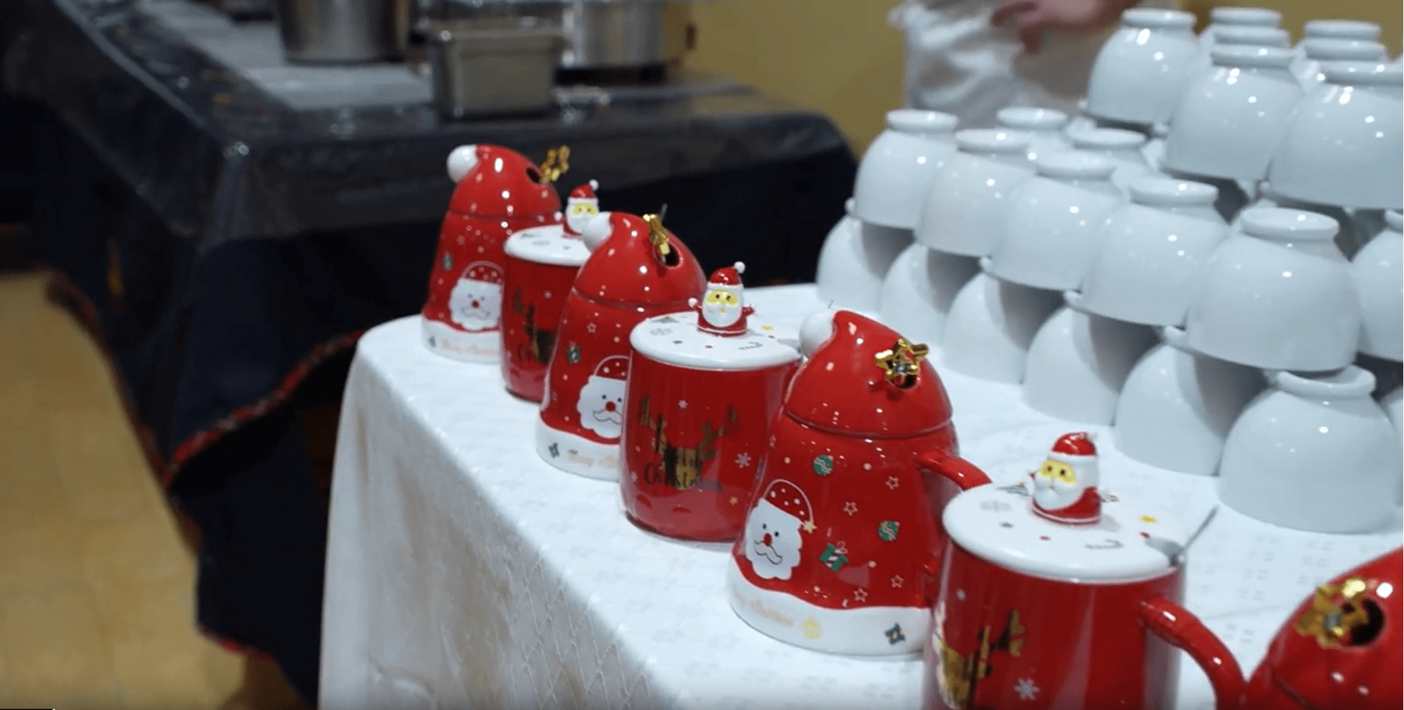 Festive red teapots with Santa motifs lined up on a table, surrounded by white cups, creating a cheerful holiday setting.