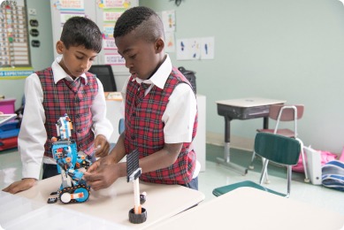 Two boys in plaid vests collaborate on building a robotic project at a classroom table. Educational, hands-on STEM activity encourages teamwork.