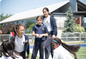 Girls participate in outdoor sports activities, smiling and interacting. One girl stands with a supportive posture, fostering teamwork and engagement.